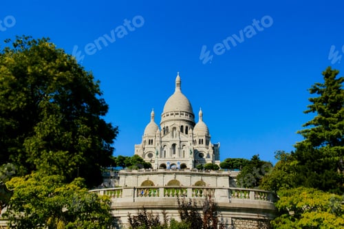 Preview: Sacré-Cœur Basilica Framed by Lush Green Trees Under a Deep Blue Sky in Montmartre, Paris
