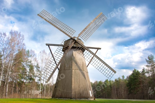 Preview: Traditional wooden windmill standing tall in a scenic countryside surrounded by pine trees and open