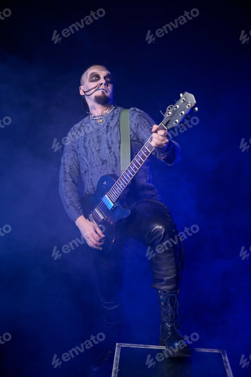 Preview: Adult male rock musician with face paint playing electric guitar on smoky stage with blue lighting