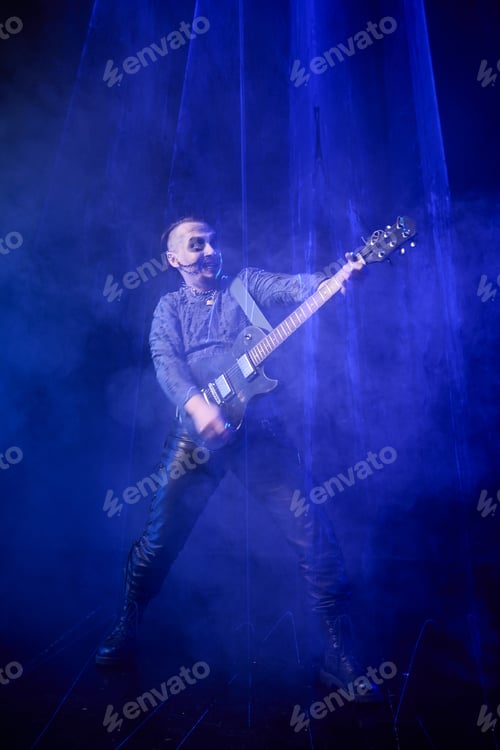 Preview: Adult man playing electric guitar on dark stage with blue spotlight and smoke effects