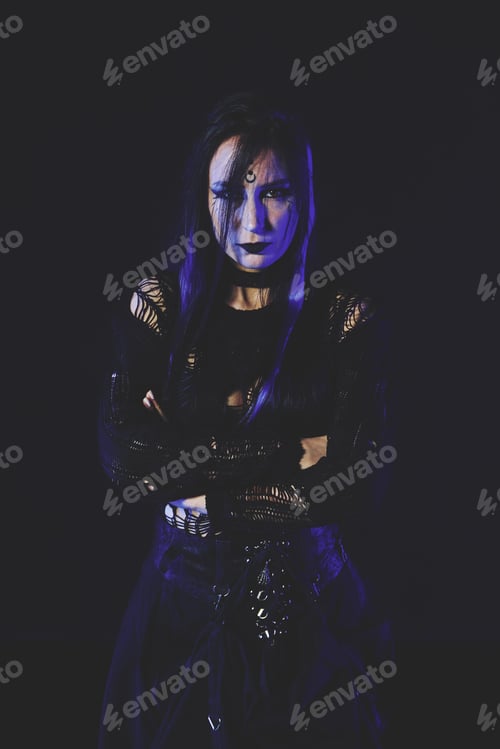 Preview: Young woman goth style with dark makeup and black lace outfit in moody low light