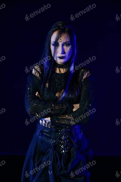 Preview: Young woman gothic style dark makeup black ripped top corset skirt blue lighting