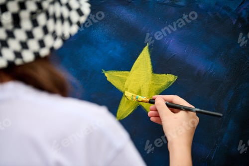 Preview: Artist painting yellow star on dark blue canvas with focused brush strokes