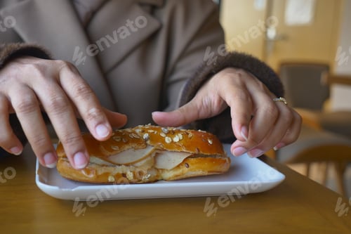 Preview: Woman enjoys bread roll at a table in a cafe