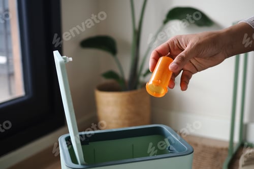 Preview: Hand puts orange container into green trash bin