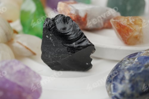 Preview: Black stone among colorful gems on white surface