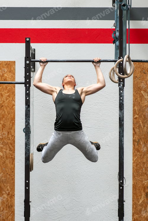 Preview: Female athlete performing kipping pull up exercise in gym