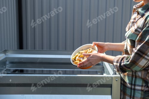 Preview: Loading vegetable and kitchen scraps into compost bin, metal frame for garden compost preparation, e