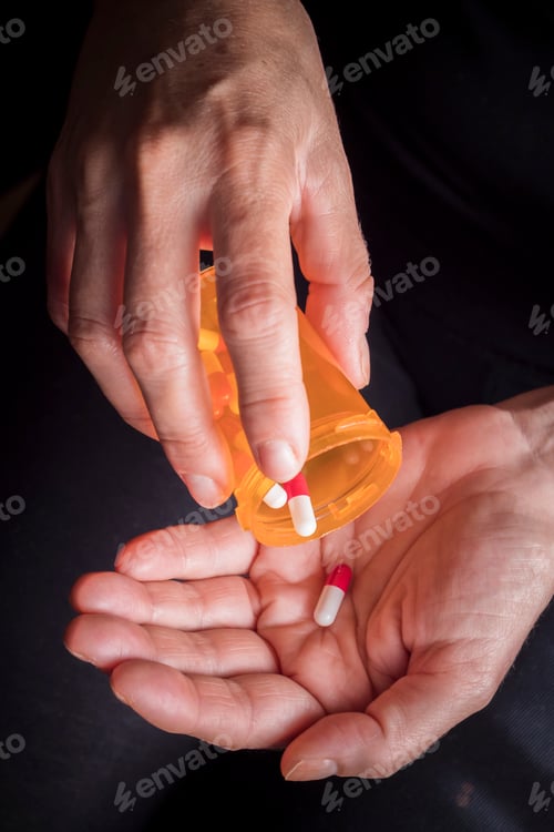 Preview: Women take white and red capsule with right hand from a ambar bottle on black background