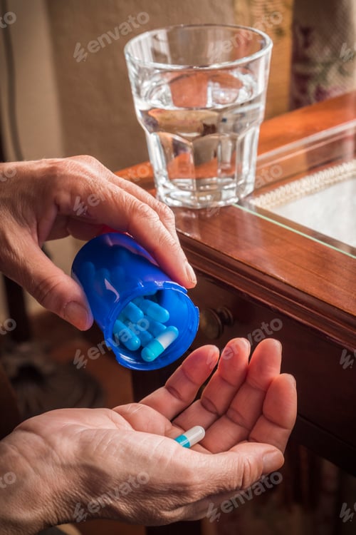 Preview: Women take white and blue capsule with left hand from a blue bottle