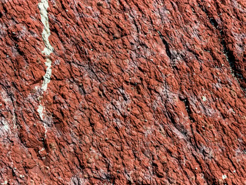 Preview: Close-up texture of natural red stone with white mineral veins.