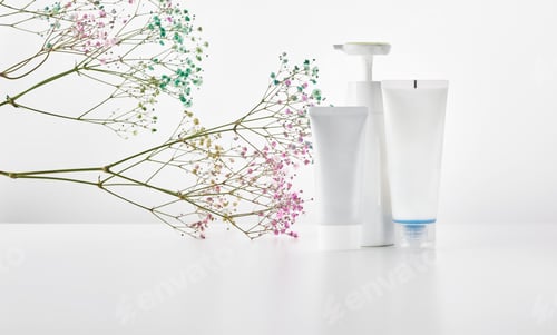Preview: A set of white cosmetic tubes and a bottle with a dispenser stand on a light surface next to branche