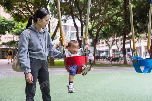 Preview: Happy mother pushing her little son on a swing in the park