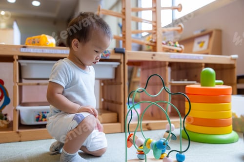 Preview: Smart baby boy sliding wooden beads along a colorful wire track indoor