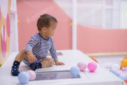 Preview: Cute toddler boy sitting on soft white play mat in indoor playground