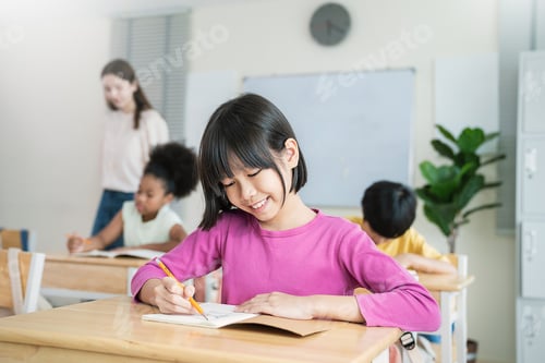 Preview: Portrait of smile little pupil writing at desk in classroom at the elementary school