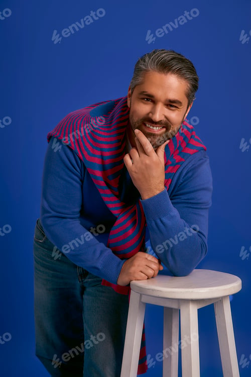 Preview: Stylish man poses confidently with a playful smile against a vibrant blue background