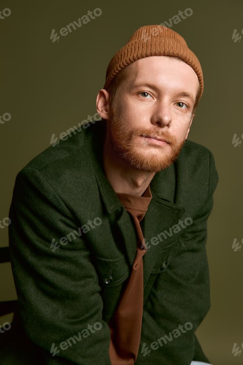 Preview: Stylish young man with a trendy hat poses confidently against a green backdrop
