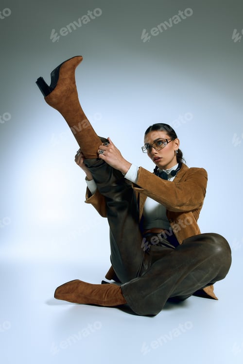 Preview: Fashionable young woman poses confidently in grey studio with her trendy suede outfit