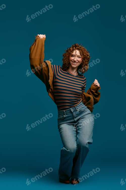 Preview: Stylish young woman expressing joy in a vibrant blue setting while showing off her fashion sense