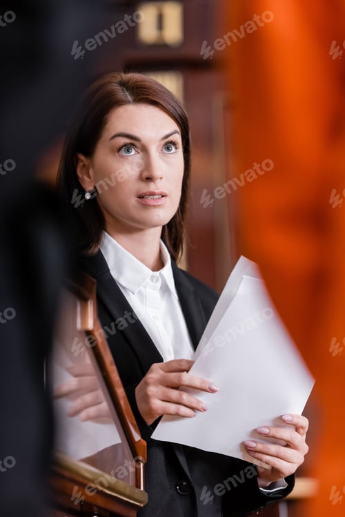 Preview: Brunette Lawyer Holding Documents in Courtroom on Blurred Foreground