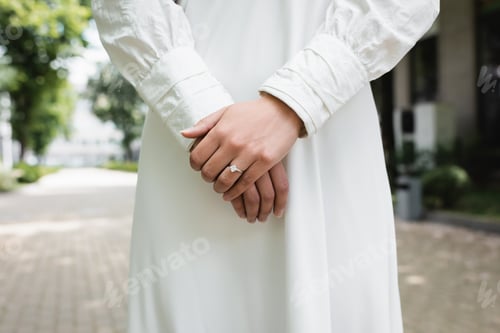 Preview: Cropped View of Bride in White Wedding Dress With Diamond Ring on Finger Standing Outside