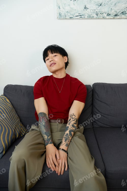 Preview: Young handsome man with tattoos relaxing on a stylish couch in a modern space
