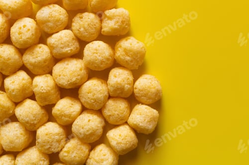 Preview: Top View of Puffed and Salty Cheese Pops on Yellow