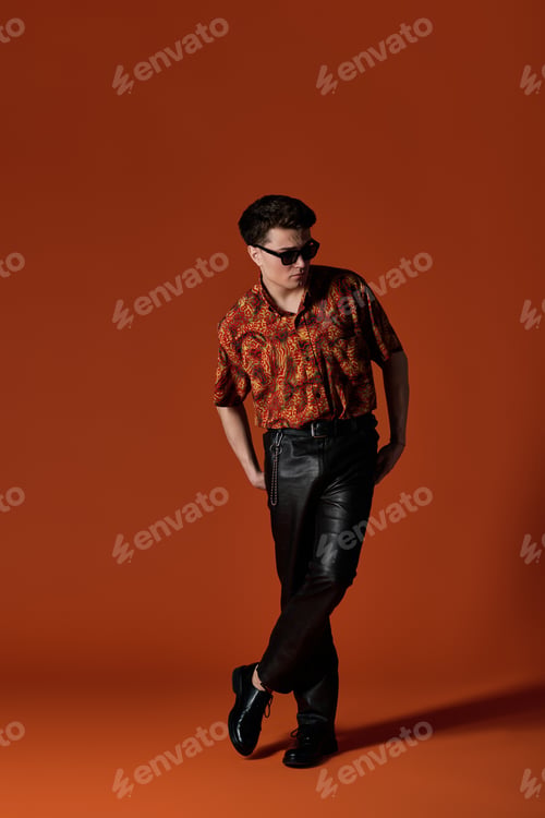 Preview: Stylish young man showcasing confidence in vibrant attire against a bold orange backdrop