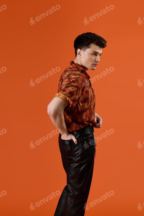 Preview: Stylish young man poses confidently in vibrant clothes against a bold orange backdrop