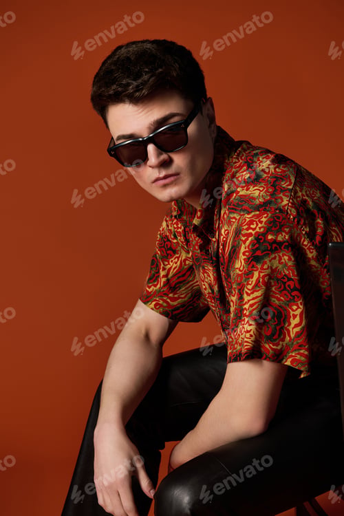 Preview: Handsome young man posing confidently in vibrant shirt against a warm orange background
