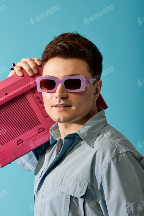 Preview: Stylish young man enjoying summer vibes with a retro boombox under a bright blue backdrop
