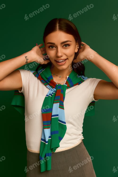 Preview: Stylish young woman poses confidently in vibrant green studio wearing a trendy outfit