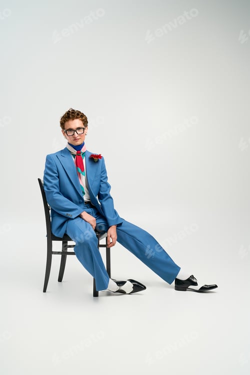 Preview: Young man showcases bold outfit choices while sitting confidently on a chair in studio