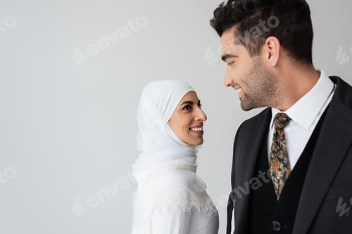 Preview: Happy Woman in Wedding Dress and Hijab Standing Near Joyful Husband in Suit Isolated on Grey