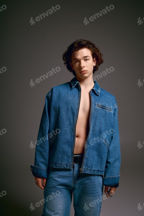 Preview: Emotional young man with curly hair showcases fashion in a stylish denim outfit