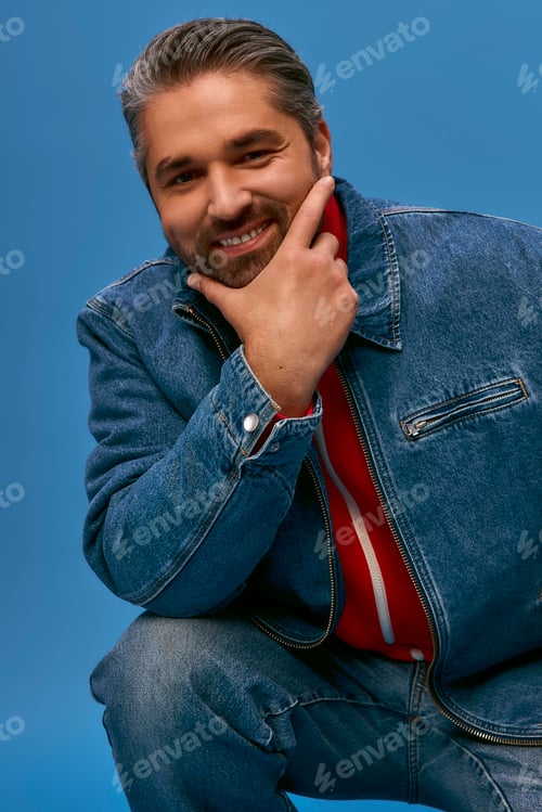 Preview: Stylish man posing confidently in casual denim attire against a vibrant blue background