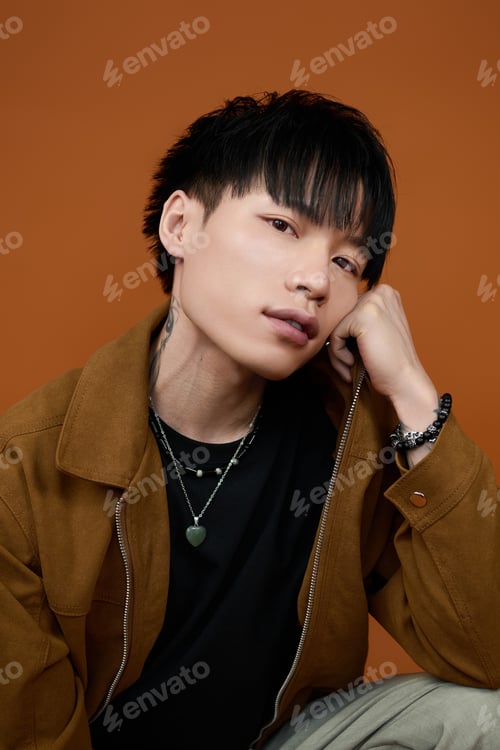 Preview: Young man with stylish hair showcases charm against warm orange backdrop