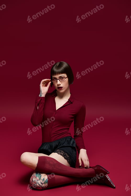 Preview: Fashionable young woman sitting stylishly against a bold red backdrop with confident expression