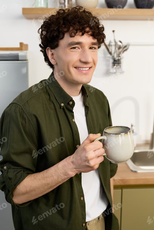 Preview: Curly young man enjoys a cozy moment with a warm drink in a stylish apartment