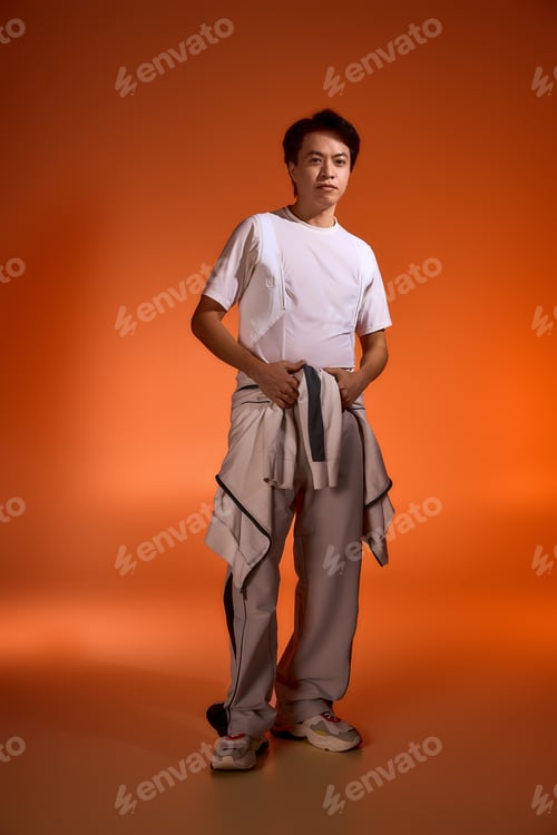Preview: Stylish young man in minimalistic outfit showcases contemporary fashion in studio
