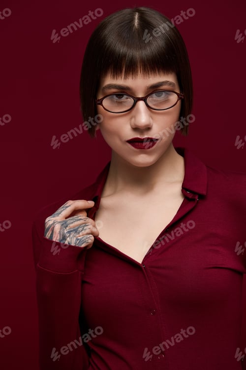 Preview: Stylish young woman with striking features poses confidently against a deep red backdrop