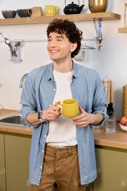 Preview: Curly young man enjoying a cozy moment in his modern apartment kitchen