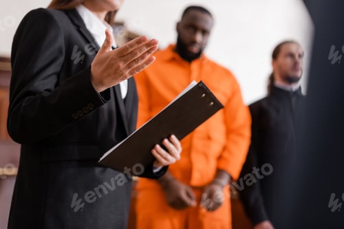 Preview: Prosecutor With Clipboard Pointing With Hand Near Accused African American Man on Blurred Background