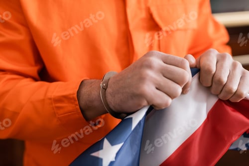 Preview: Partial View of Convicted Man in Handcuffs and Jail Uniform Tearing Usa Flag, Justice Concept