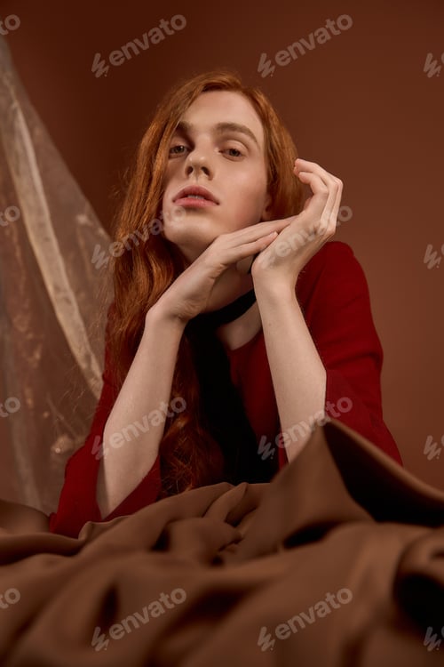 Preview: Handsome young man with long red hair showcases elegant fashion in a warm, artistic setting