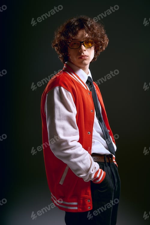 Preview: Young handsome man with curly hair displays emotion in stylish attire against dark backdrop