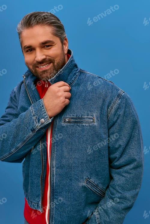 Preview: Stylish man poses confidently in a denim jacket against a vibrant blue backdrop