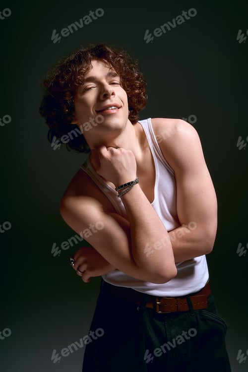 Preview: Charming young man with curly hair exudes emotion in stylish fashion studio setting