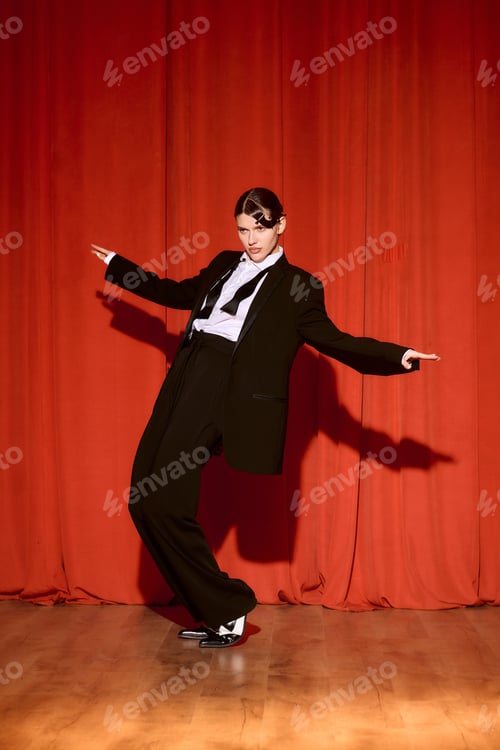 Preview: Captivating performance of a young woman in a sleek suit on stage under vibrant red curtains